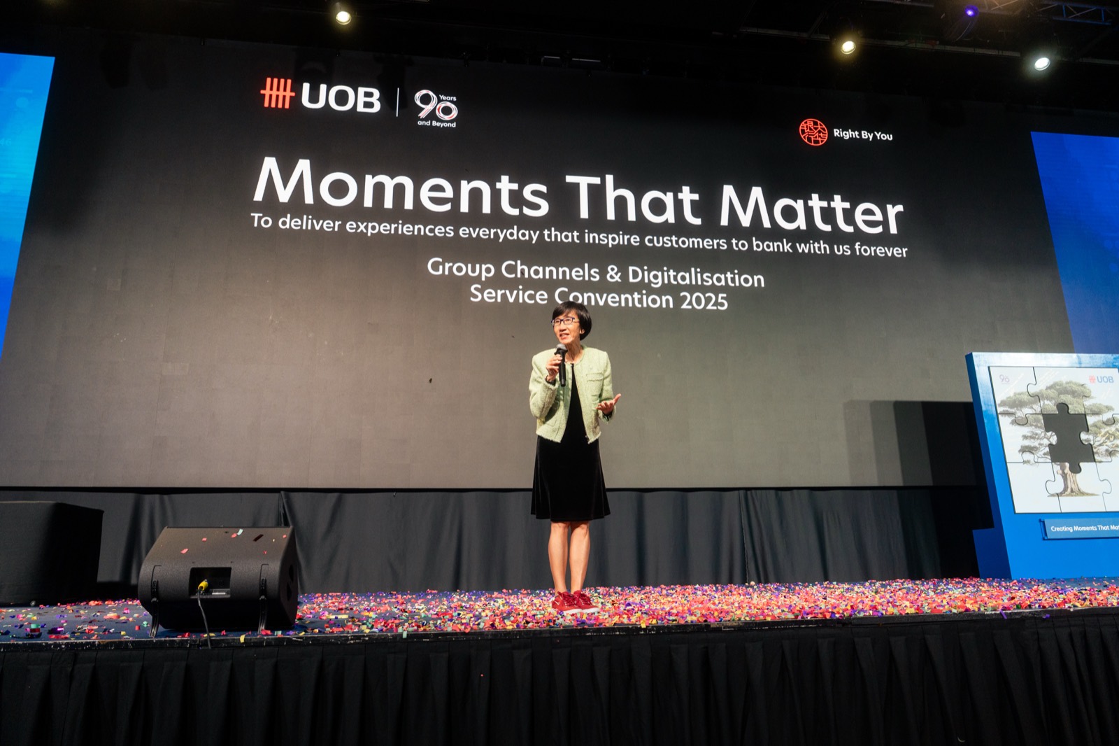 Speaker on a confetti-covered stage under the words Moments That Matter at UOB's service convention in Singapore